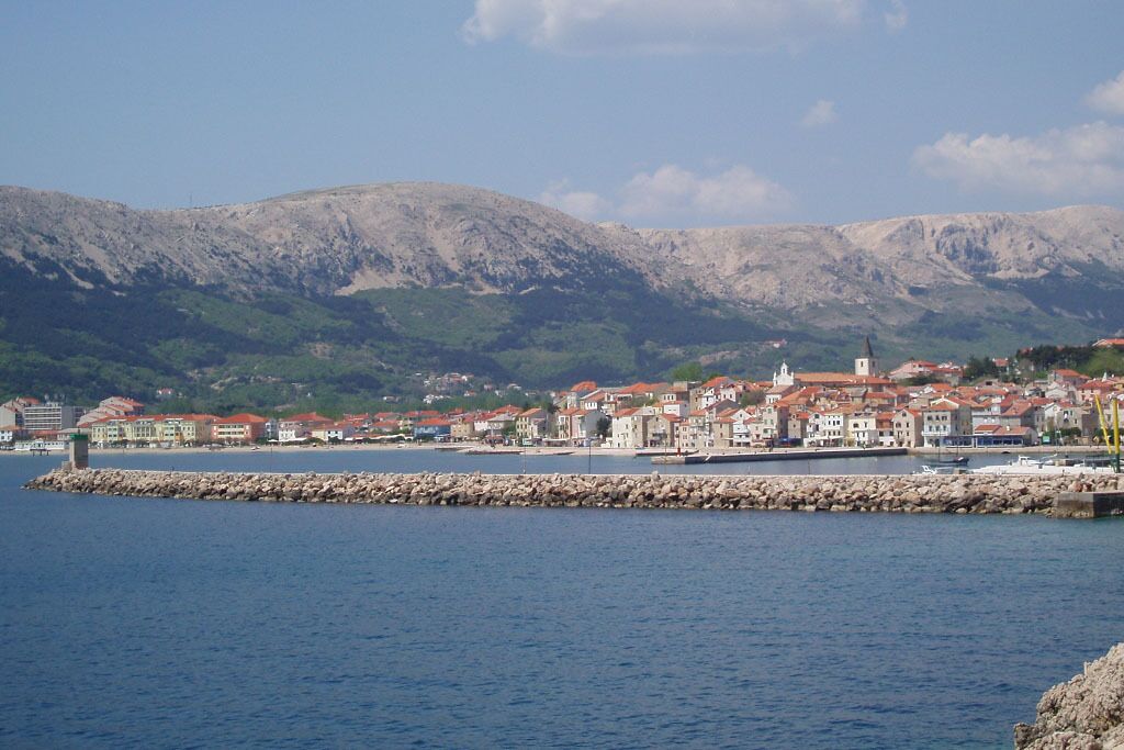 A coastal town with buildings along the waterfront, a prominent church, and mountains in the background.