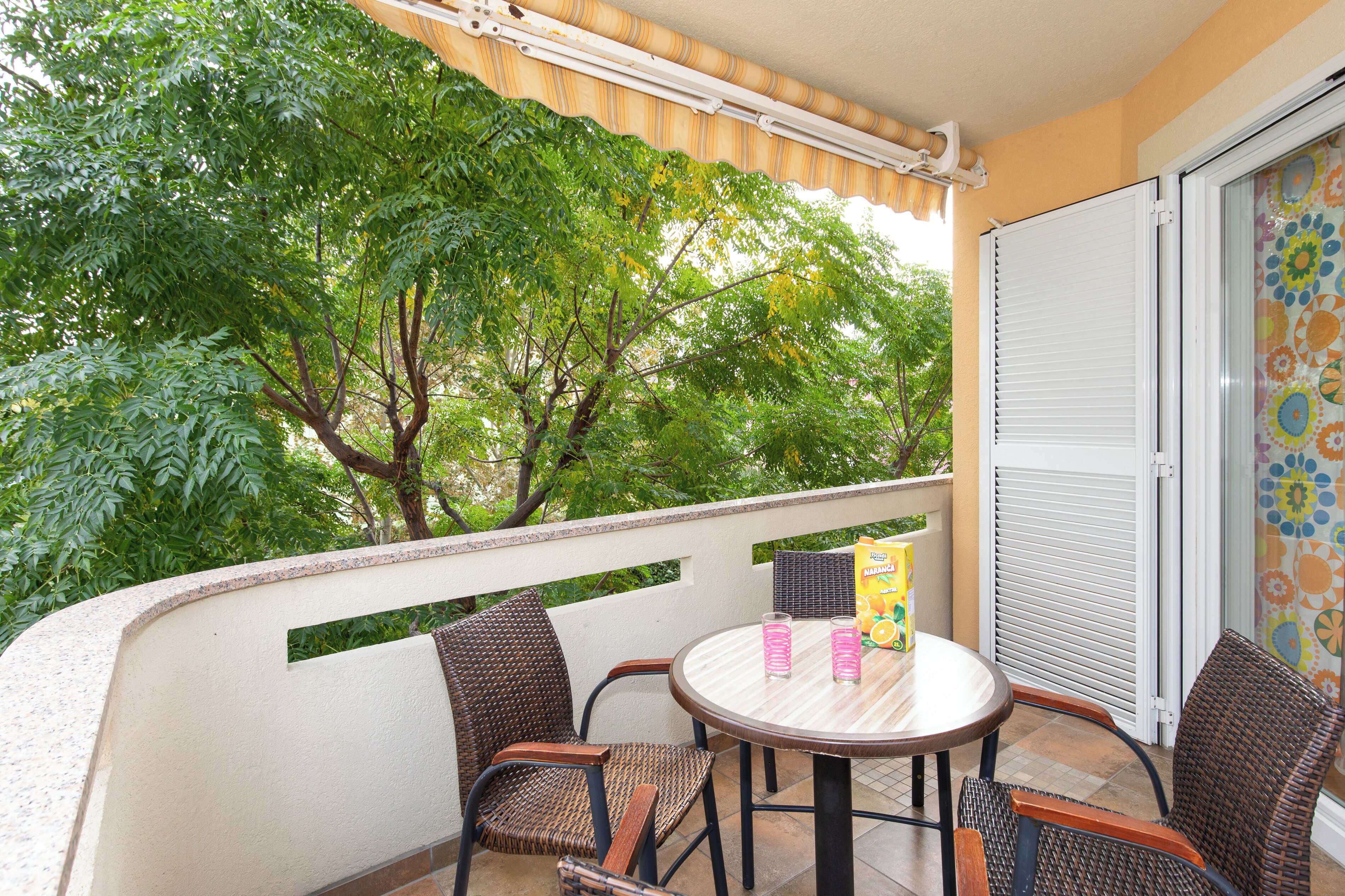 A balcony with wicker chairs, a round table, and a box of orange juice.