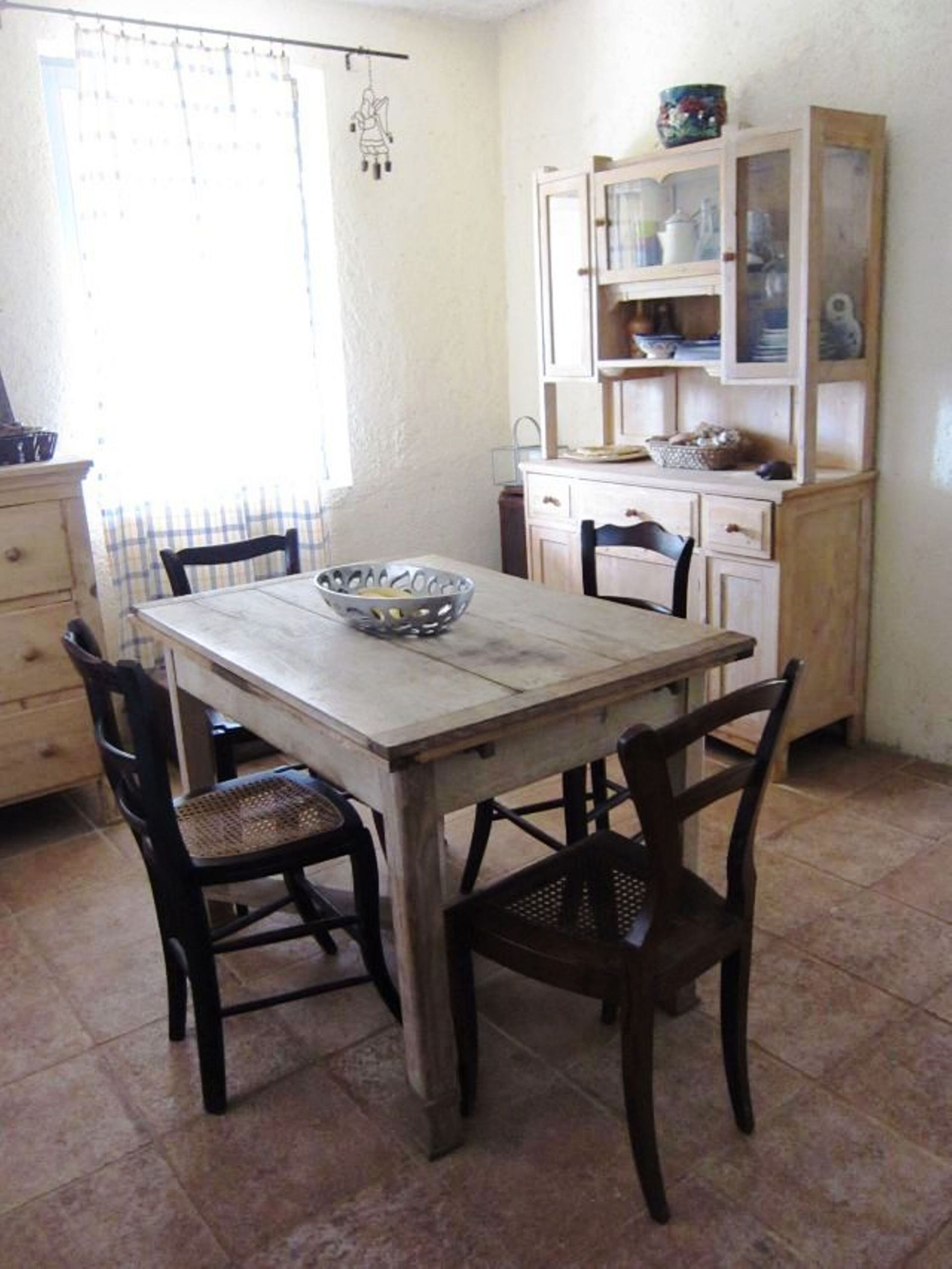 Un coin repas comprenant une table en bois et quatre chaises, un meuble avec des portes en verre et une fenêtre avec un rideau.
