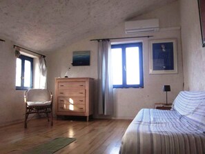 Una camera da letto con un comò in legno, un letto con copriletto a righe, una sedia e una finestra con tende.