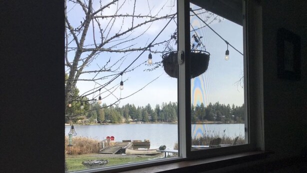 Huone, jossa on suuri ikkuna, josta avautuu näkymä järvelle, laiturille ja puulle.