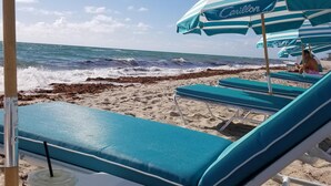Un área de descanso en la playa con sombrillas a rayas y sillones reclinables.