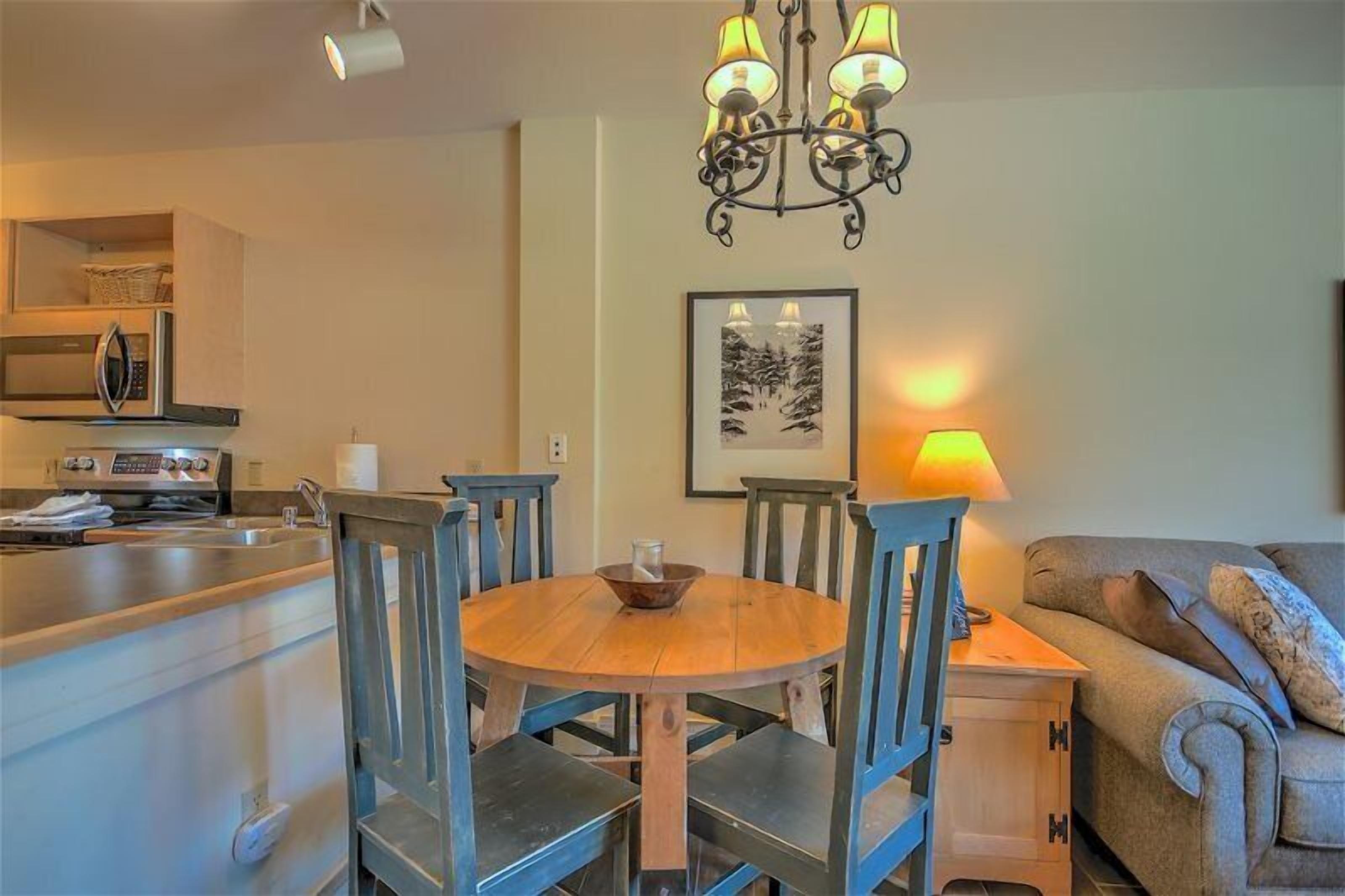 A dining area with a wooden table and chairs, a chandelier, a microwave, and a sofa.