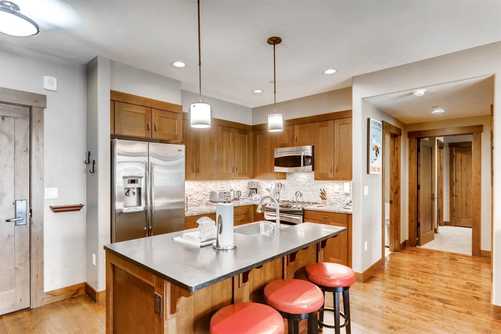 A modern kitchen with wooden cabinets, stainless steel appliances, and a central island with stools.