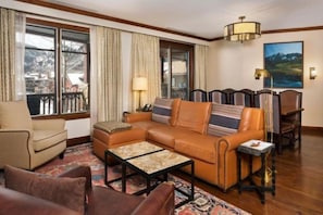 A living room with a sofa, armchairs, a coffee table, and a view of a mountainous landscape through large windows.