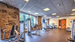A gym with various exercise machines, stone walls, and large windows.