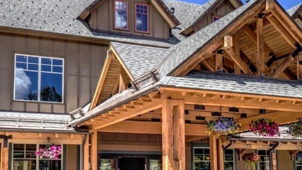 A wooden lodge with a covered entrance, large windows, and a stone fireplace.