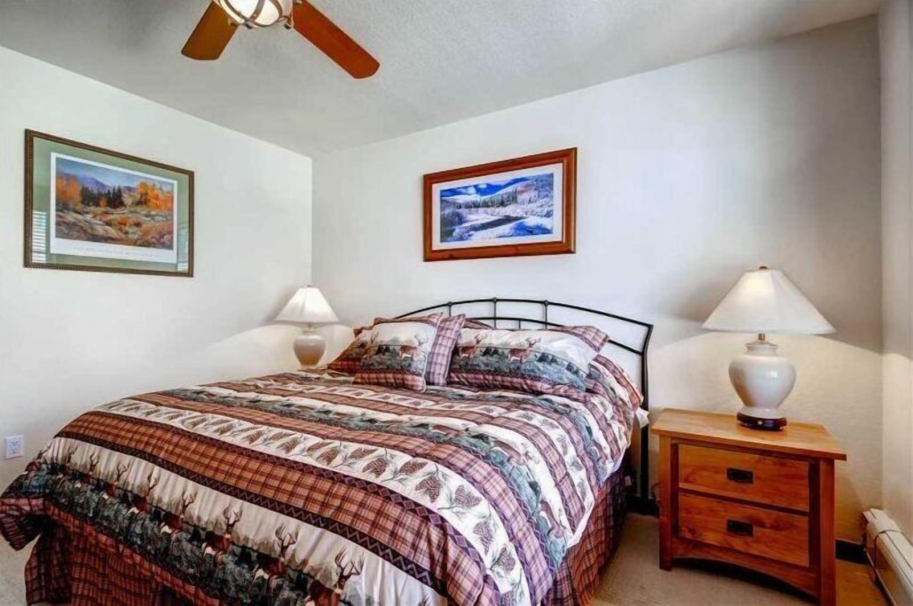 Un dormitorio con una cama, dos lámparas de noche, una mesita de noche y dos cuadros en la pared.