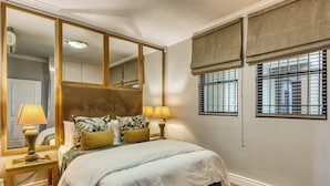 Un dormitorio con una cama grande, dos lámparas de noche, un espejo y una ventana con persianas.