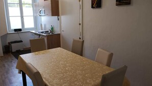 Ruokailutila, jossa on pöytä ja tuolit, keittiö, jossa on pesuallas ja kaappeja, sekä kaksi taulua seinällä.