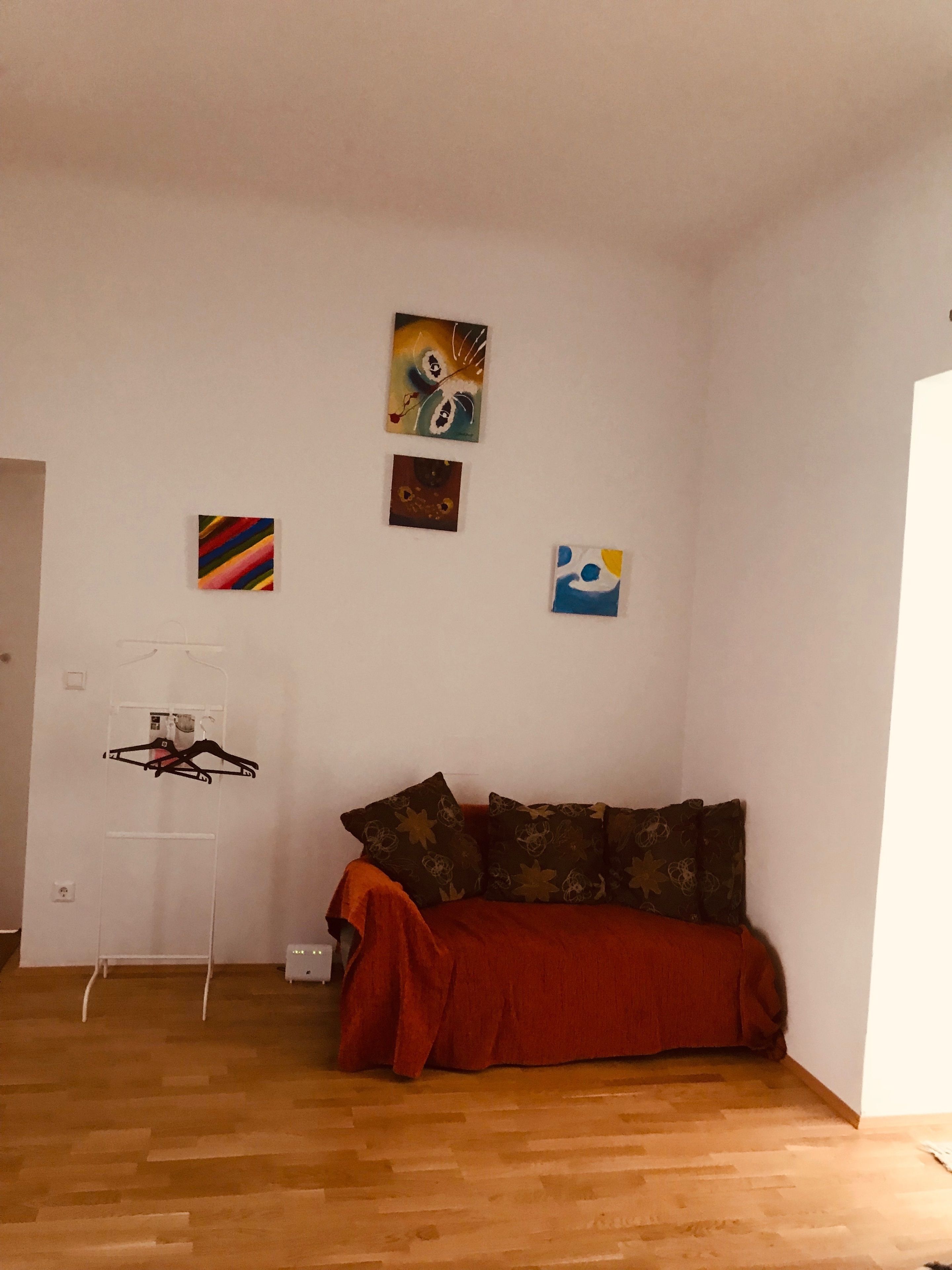 A room with a wooden floor, a red sofa, and three paintings on the wall.