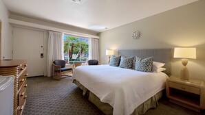 Ein Hotelzimmer mit einem großen Bett, zwei Nachttischlampen, einem kleinen Tisch, einem Stuhl und einem Fenster mit Vorhängen.