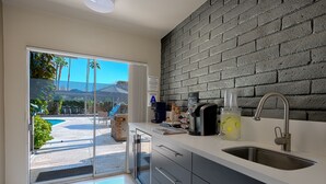 Eine moderne Küche mit großem Fenster, einer Ziegelwand und Blick auf Pool und Palmen.