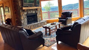 A cozy living room with a stone fireplace, leather sofas, and a large window overlooking a deck. - AWESOME View 2500 sqft decks 8 person Spa mins to Blue Ridge Pkway & New River (Fleetwood)
