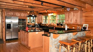 A spacious kitchen with wooden cabinets, a large island with stools, a refrigerator, oven, and a stone accent wall. - AWESOME View 2500 sqft decks 8 person Spa mins to Blue Ridge Pkway & New River (Fleetwood)