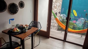 A dining area with a table set for two, a chair, and a view of a tropical mural through a sliding glass door.