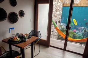 A dining area with a table set for two, a chair, and a view of a tropical mural through a sliding glass door. - Collection O Latino Boutique Tulum (Tulum)