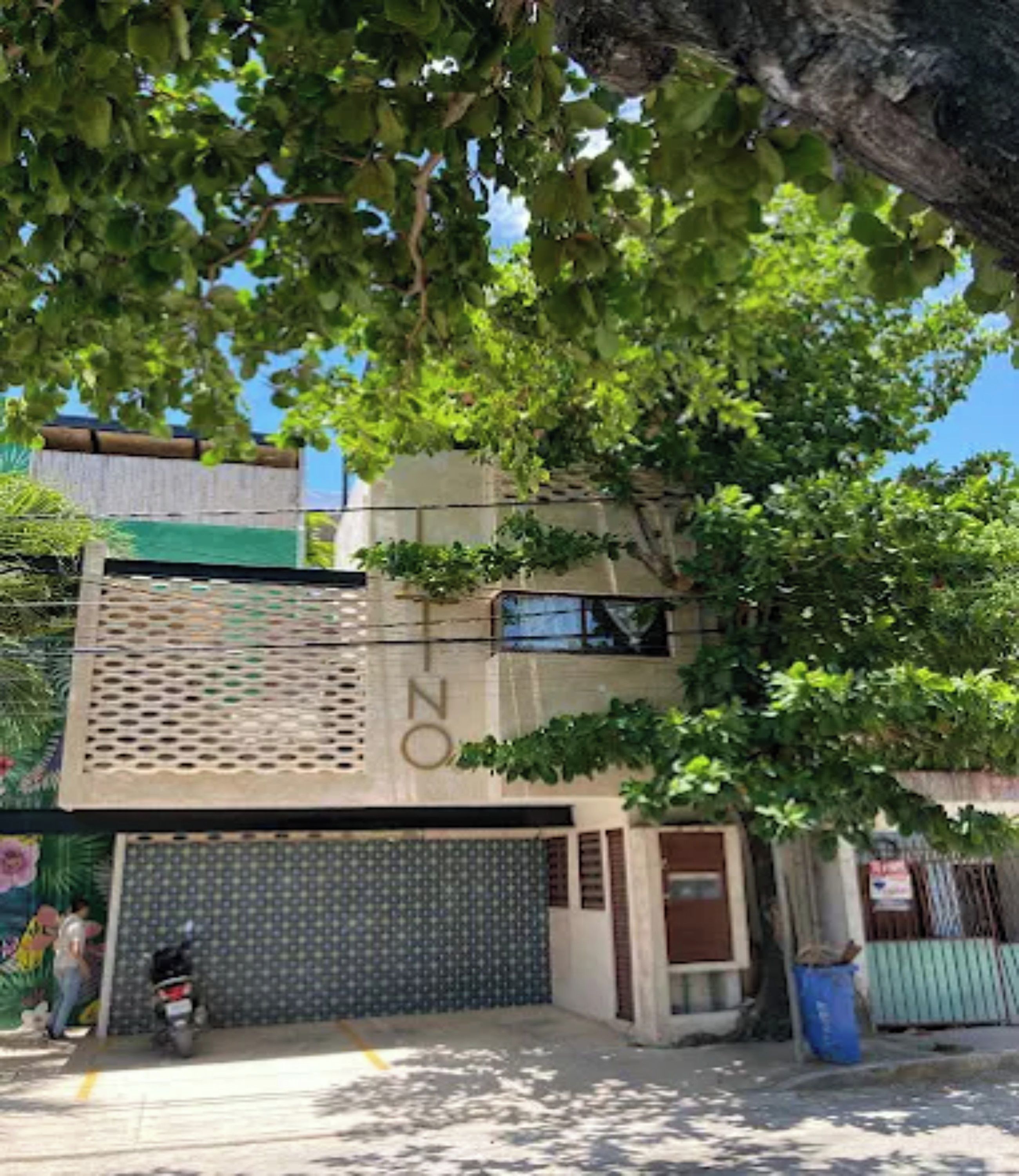 Un edificio con una puerta de garaje, un árbol en frente y una motocicleta estacionada cerca.