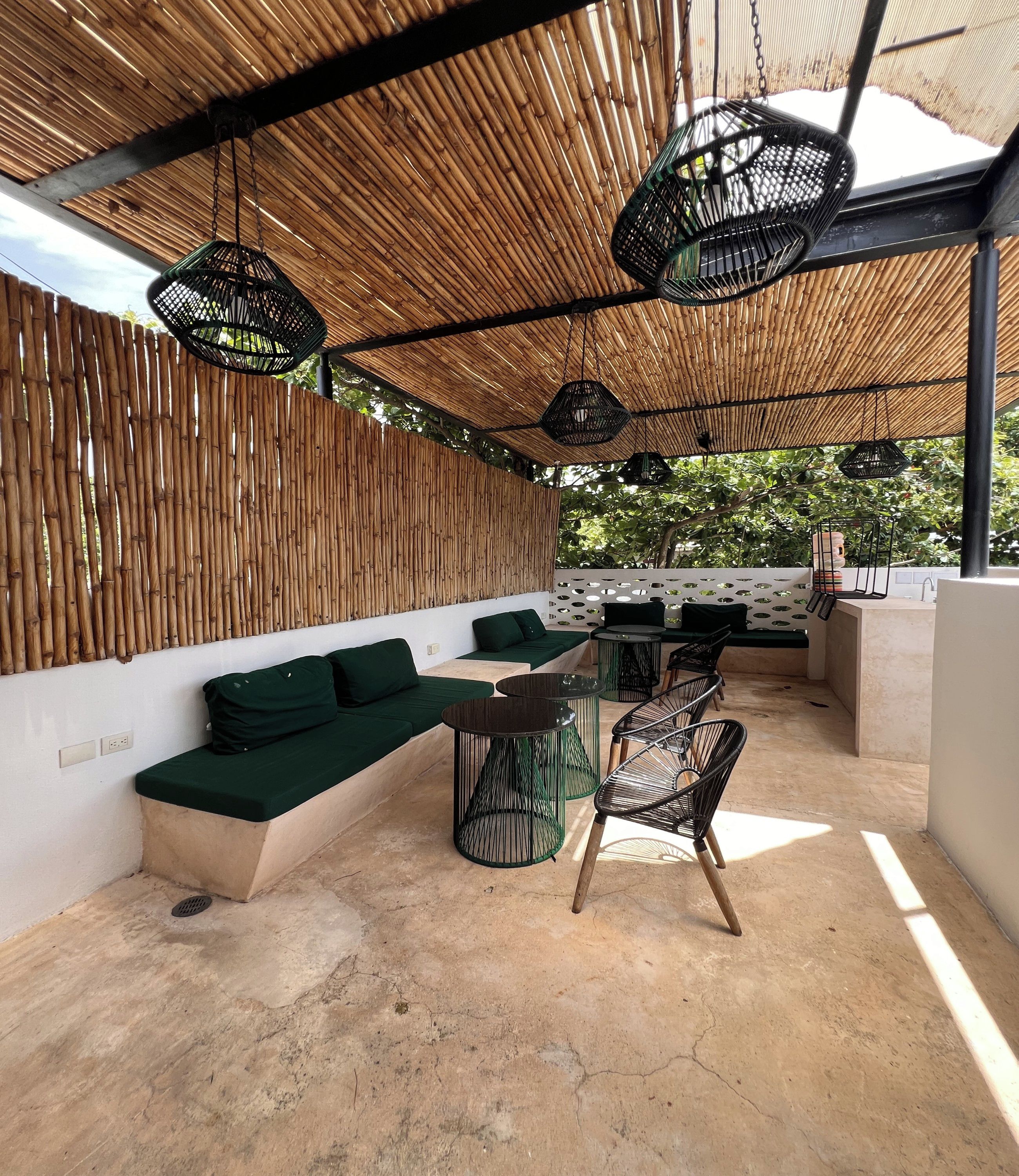 An outdoor seating area with a bamboo ceiling, green cushions, and metal chairs.