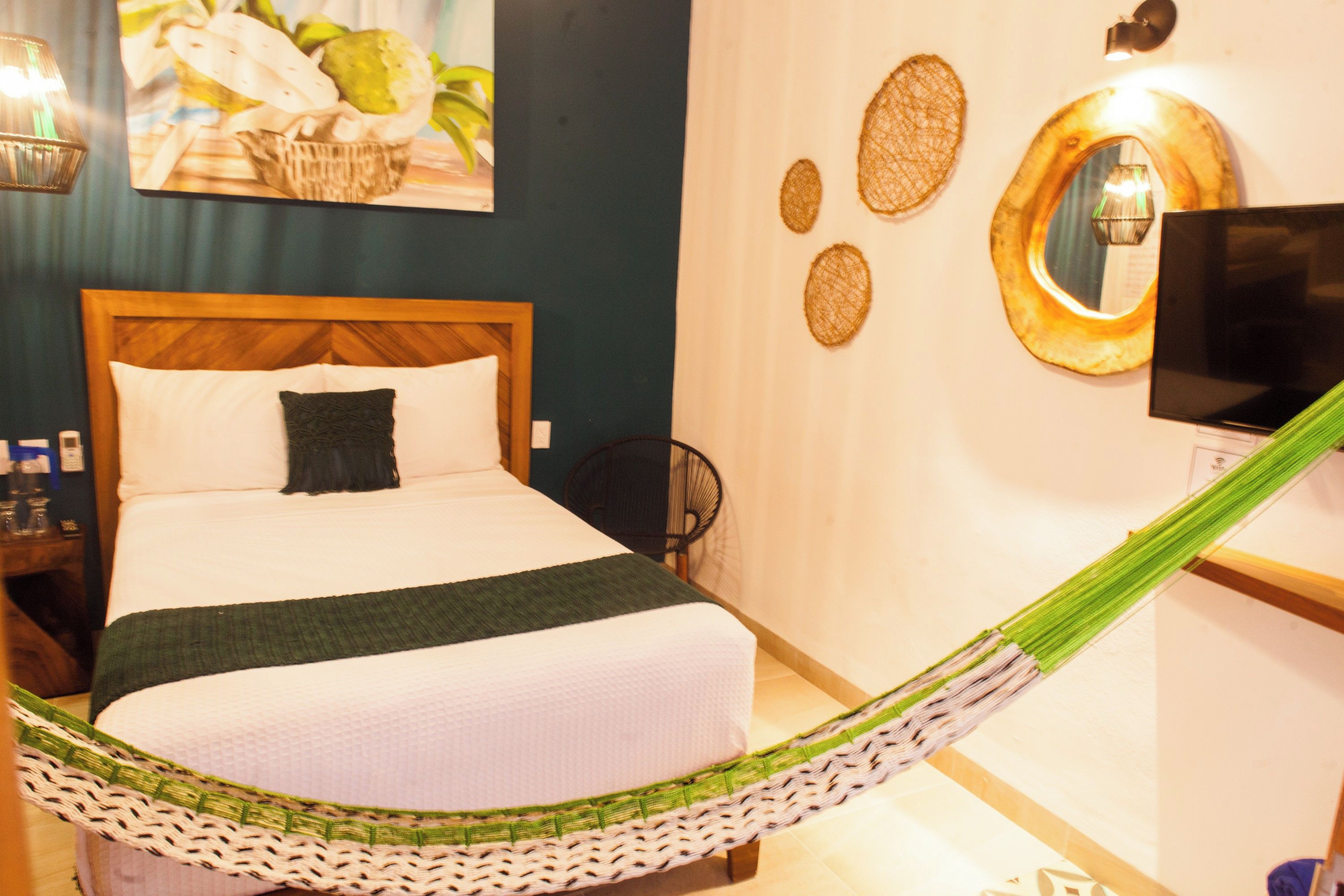A hotel room with a bed, a TV, a wall-mounted mirror, and a hammock.