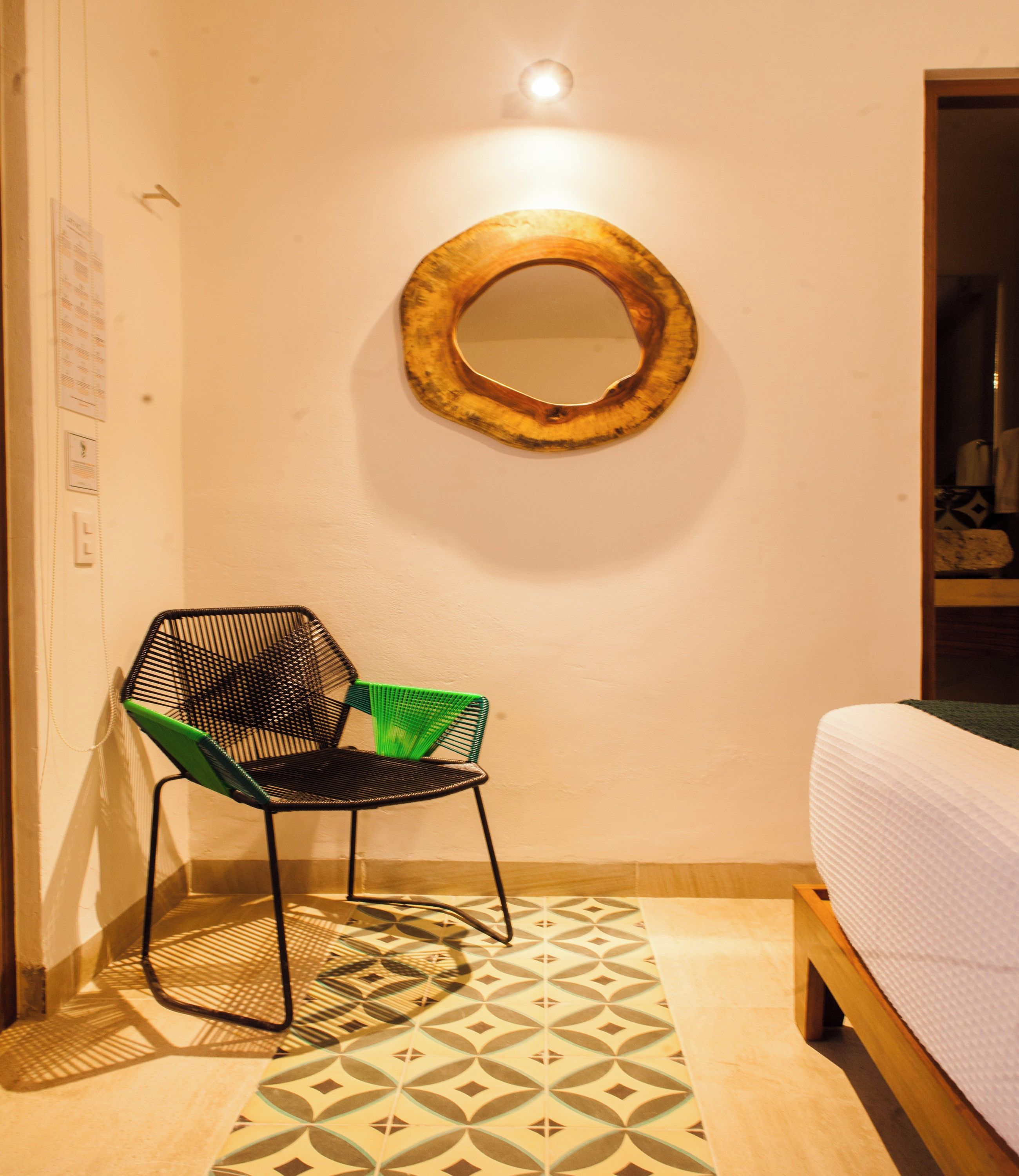 Una habitación pequeña con una cama, una silla, un espejo en la pared y baldosas de suelo estampadas.