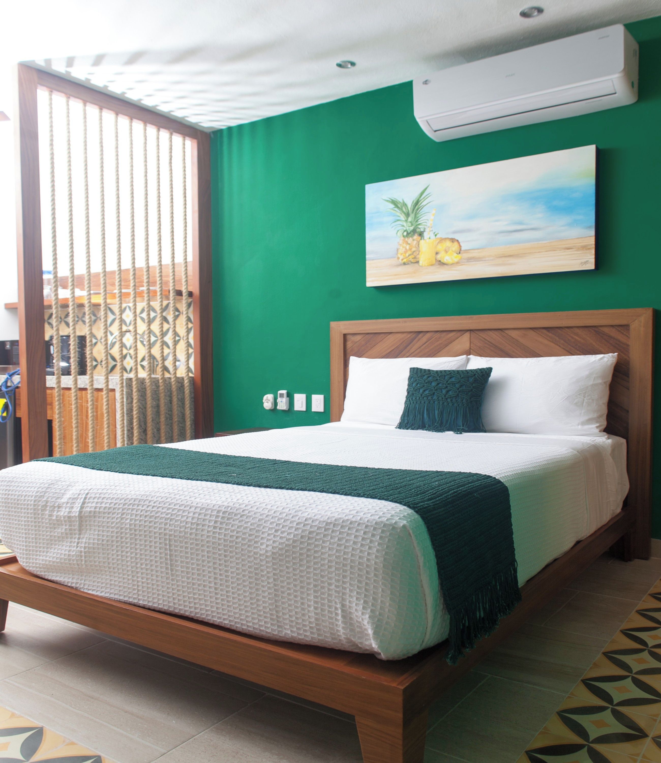 A bed with a wooden frame, a green wall, and a painting of pineapples.