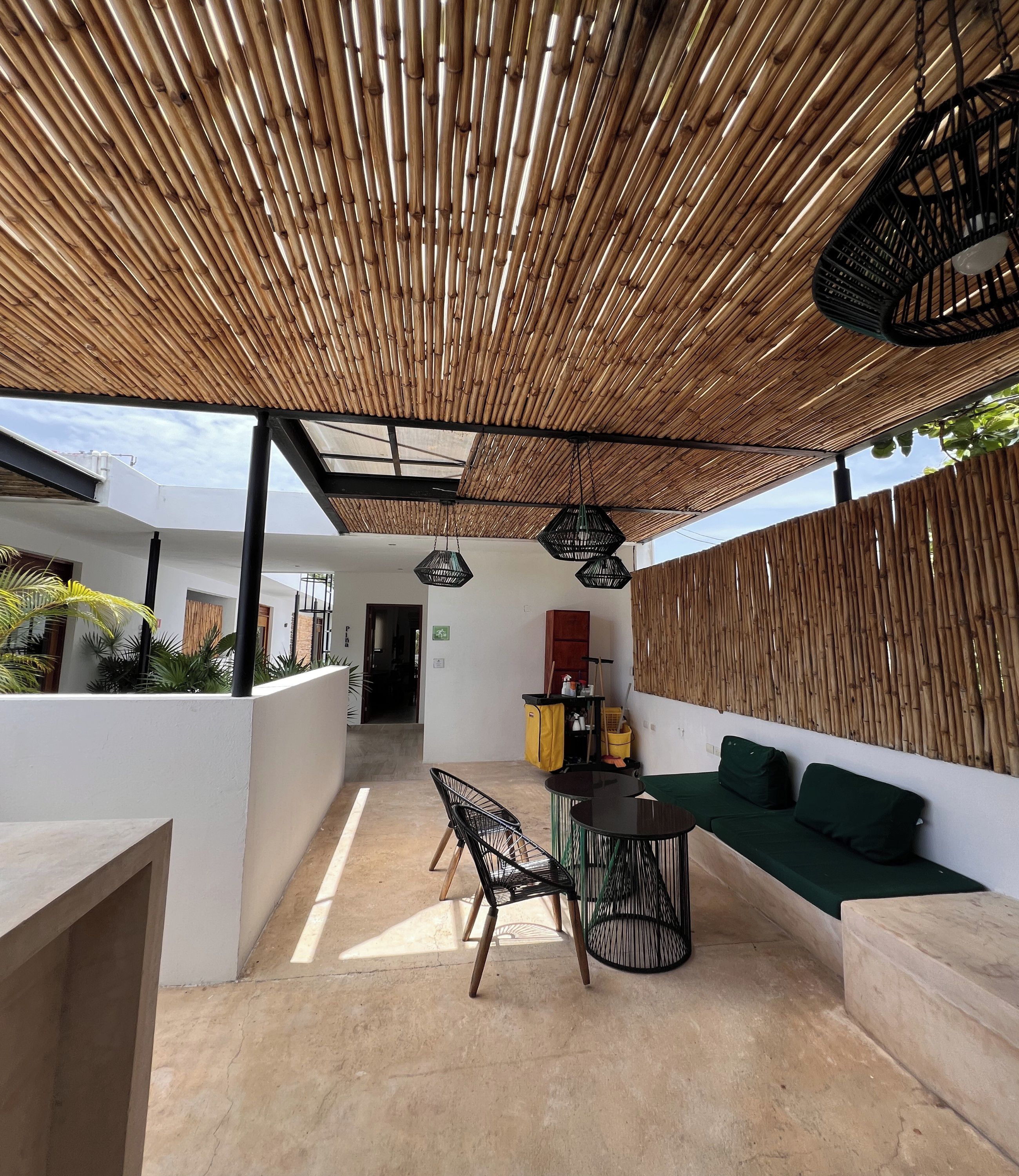 Uma área de estar coberta ao ar livre, com teto de bambu, sofá, mesa e cadeiras.