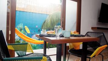 Un comedor con una mesa dispuesta para dos personas, sillas y vista al cielo azul y palmeras a través de un ventanal.