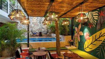 A poolside area with seating and tables, surrounded by plants and a stone wall.