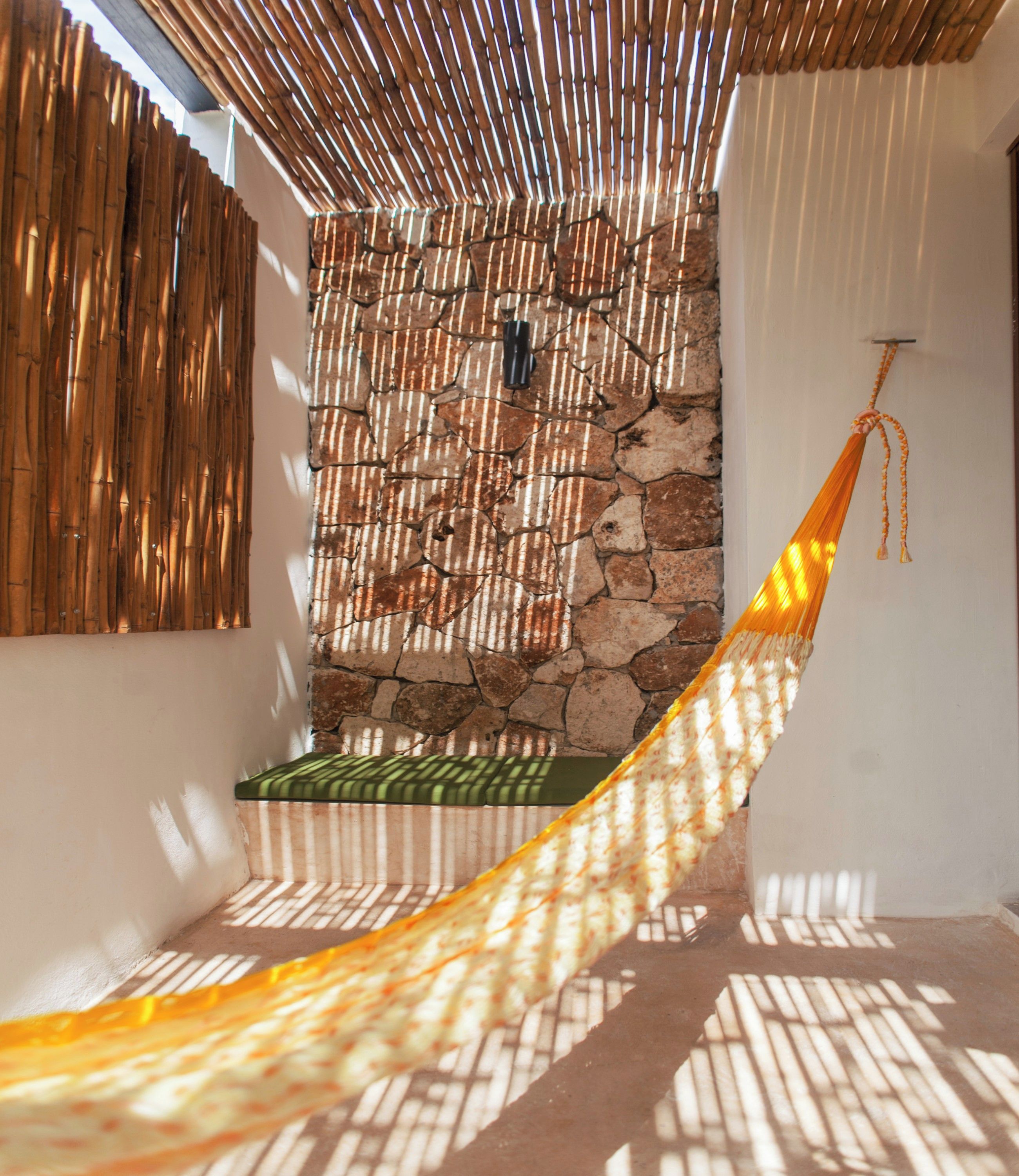 A hammock in a sunlit room with a stone wall and bamboo slats.