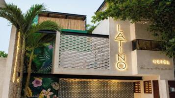 A modern building with a prominent 'LA INO HOTEL' sign, a decorative metal facade, and a tropical mural.