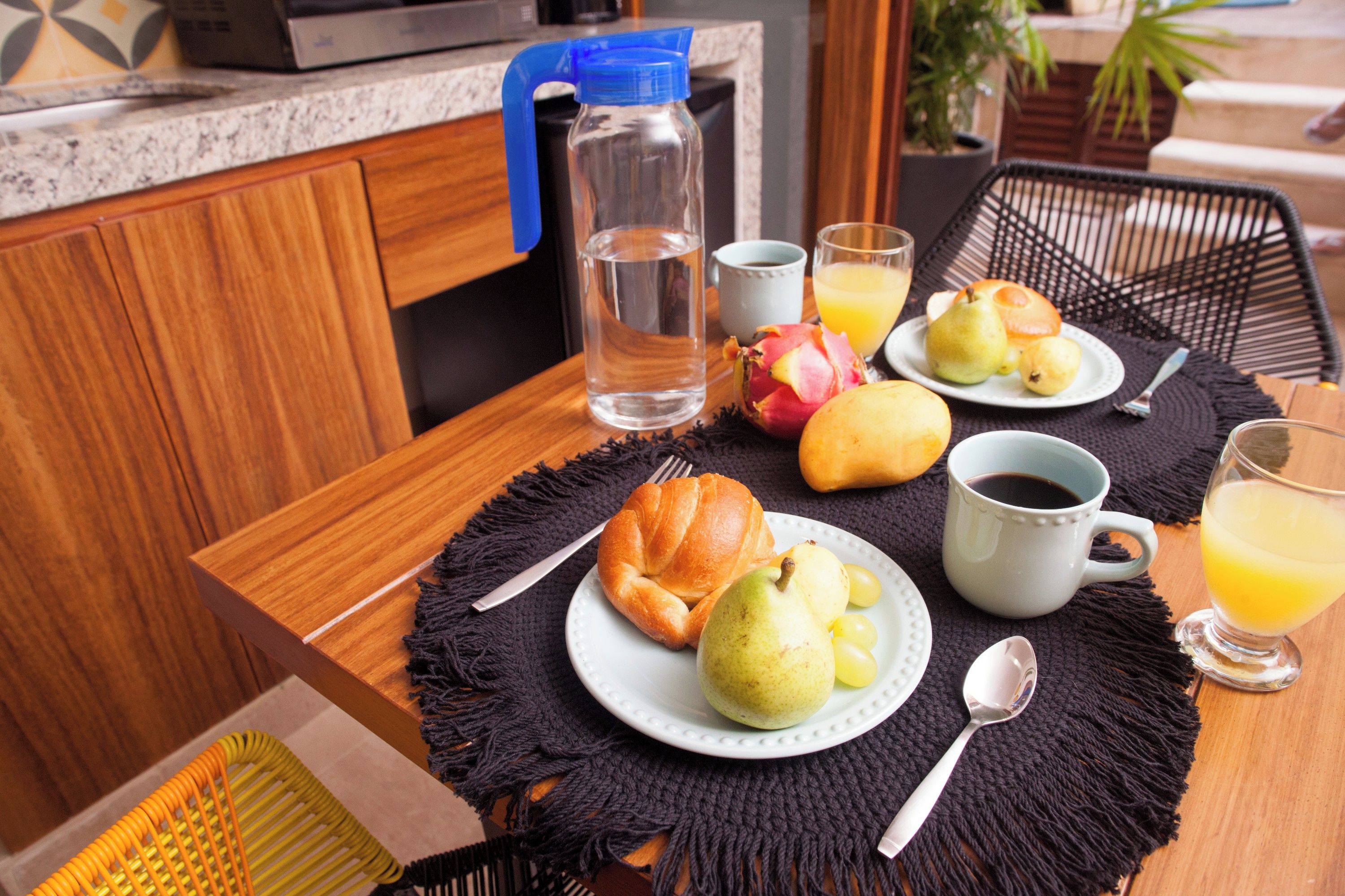 Un desayuno con un croissant, peras, un vaso de zumo de naranja y una taza de café sobre una mesa.