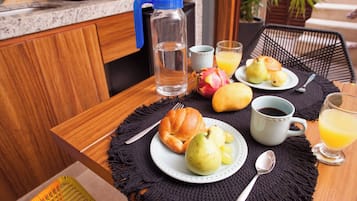 A breakfast setting with a croissant, pears, a glass of orange juice, and a coffee cup on a table.