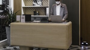 Un mostrador de recepción moderno con una laptop, una planta en maceta y un cuadro en la pared.