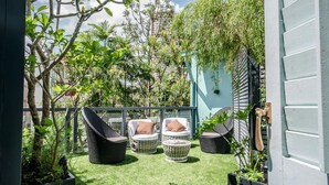 Un patio con muebles de mimbre, una mesa redonda pequeña y macetas con plantas.