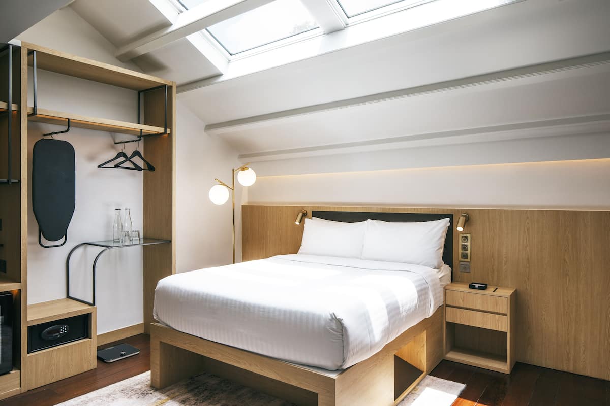 A modern bedroom with a skylight, a bed with white bedding, a bedside table, and a wardrobe with a mirror and hanging clothes.