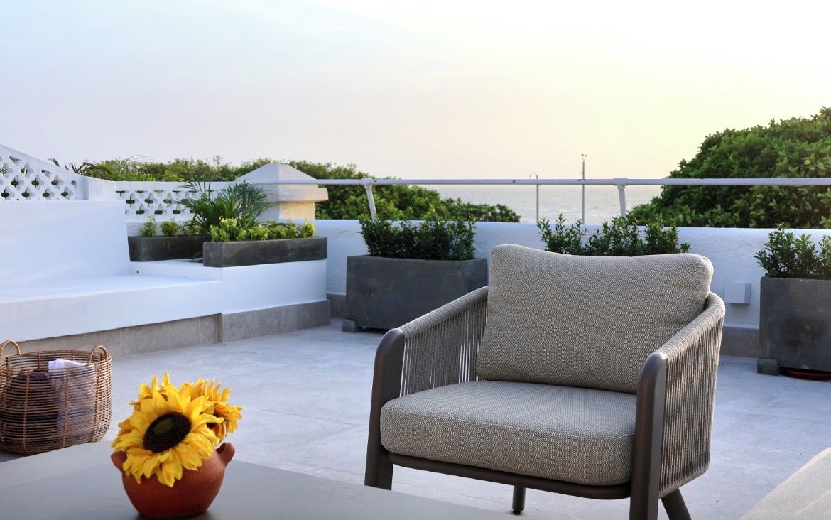 Eine Dachterrasse mit Korbstuhl, Terrakottatopf mit Sonnenblumen und Topfpflanzen.