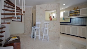 A kitchen with white cabinets, a tiled backsplash, and a dining area with two white stools.