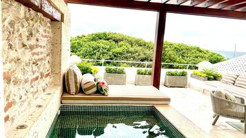 A pool area with a tiled floor, a bench with cushions, and a view of a green landscape.