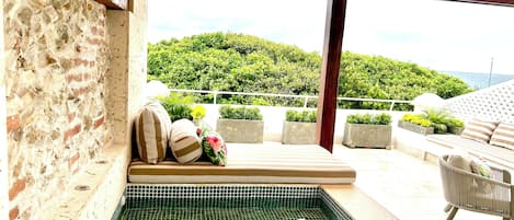 A pool area with a tiled floor, a bench with cushions, and a view of a green landscape.
