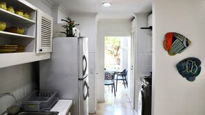 A kitchen with white cabinets, a refrigerator, and a sink. There is a dining area with a table and chairs visible through an open door. - Colonial townhouse in the Old City with panoramic ocean views (Cartagena)