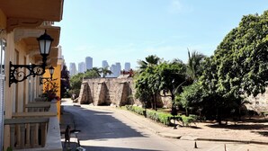 A street with a stone wall, a lamp post, and a building with a balcony.