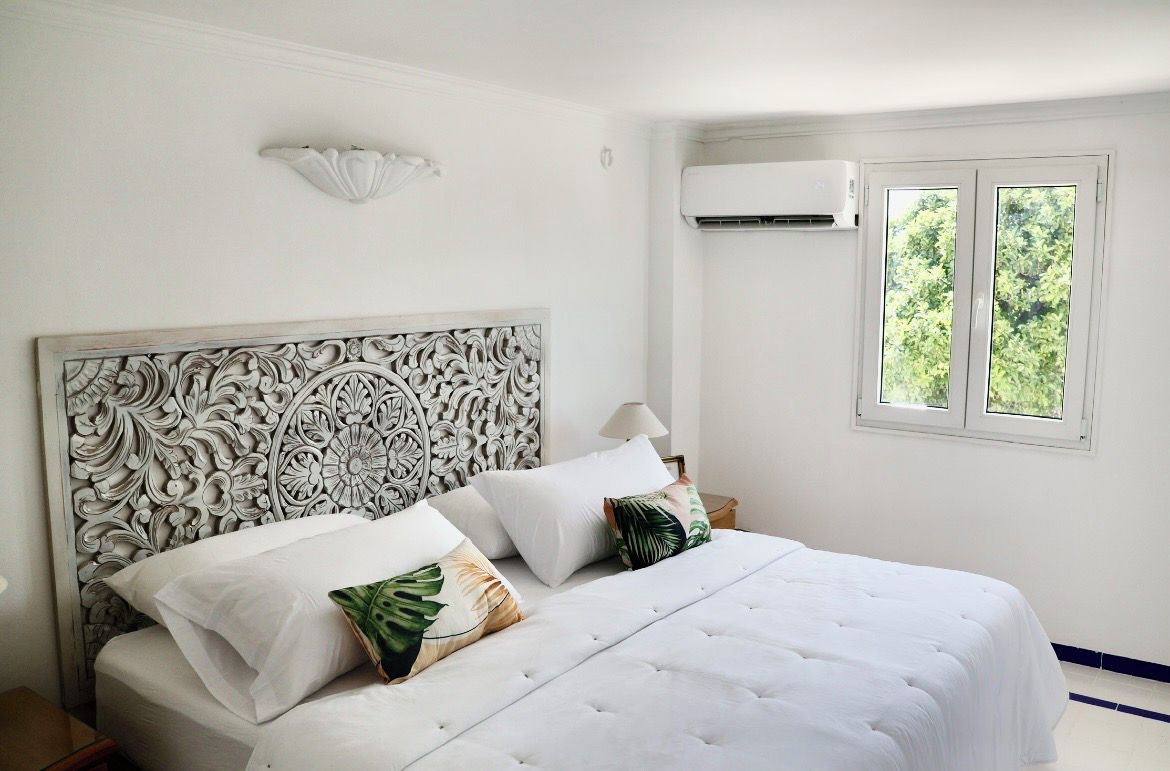 A bedroom with a white bed, decorative headboard, and a window with a view of trees.