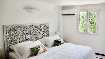A bedroom with a white bed, decorative headboard, and a window with a view of trees.