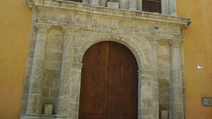 A historic building with a large wooden door, arched windows, and a statue above the door. - Colonial townhouse in the Old City with panoramic ocean views (Cartagena)