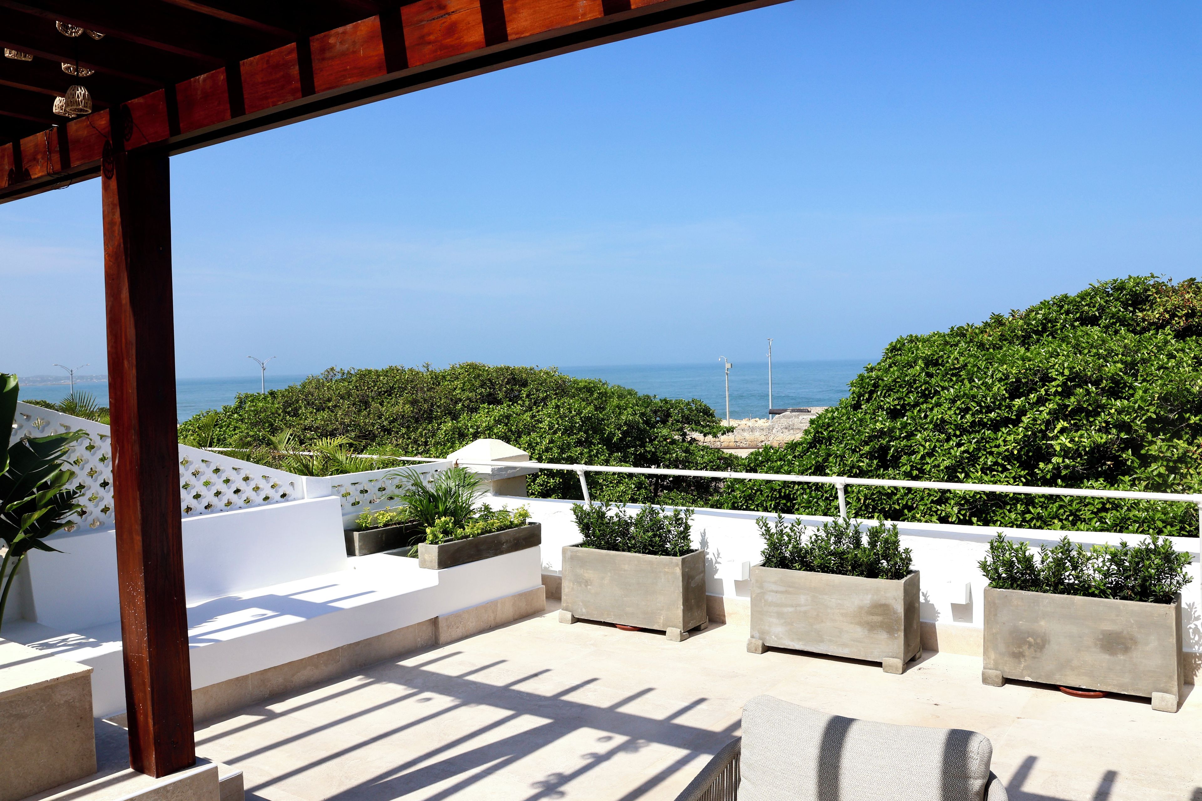 Une terrasse offrant une vue sur la mer, entourée de verdure et agrémentée de rampes blanches.