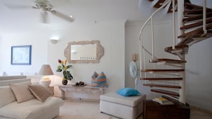 A living room with a white sofa, a small table with a lamp, a mirror, and a staircase.