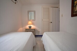Two single beds with white duvets, a bedside table, and a lamp.