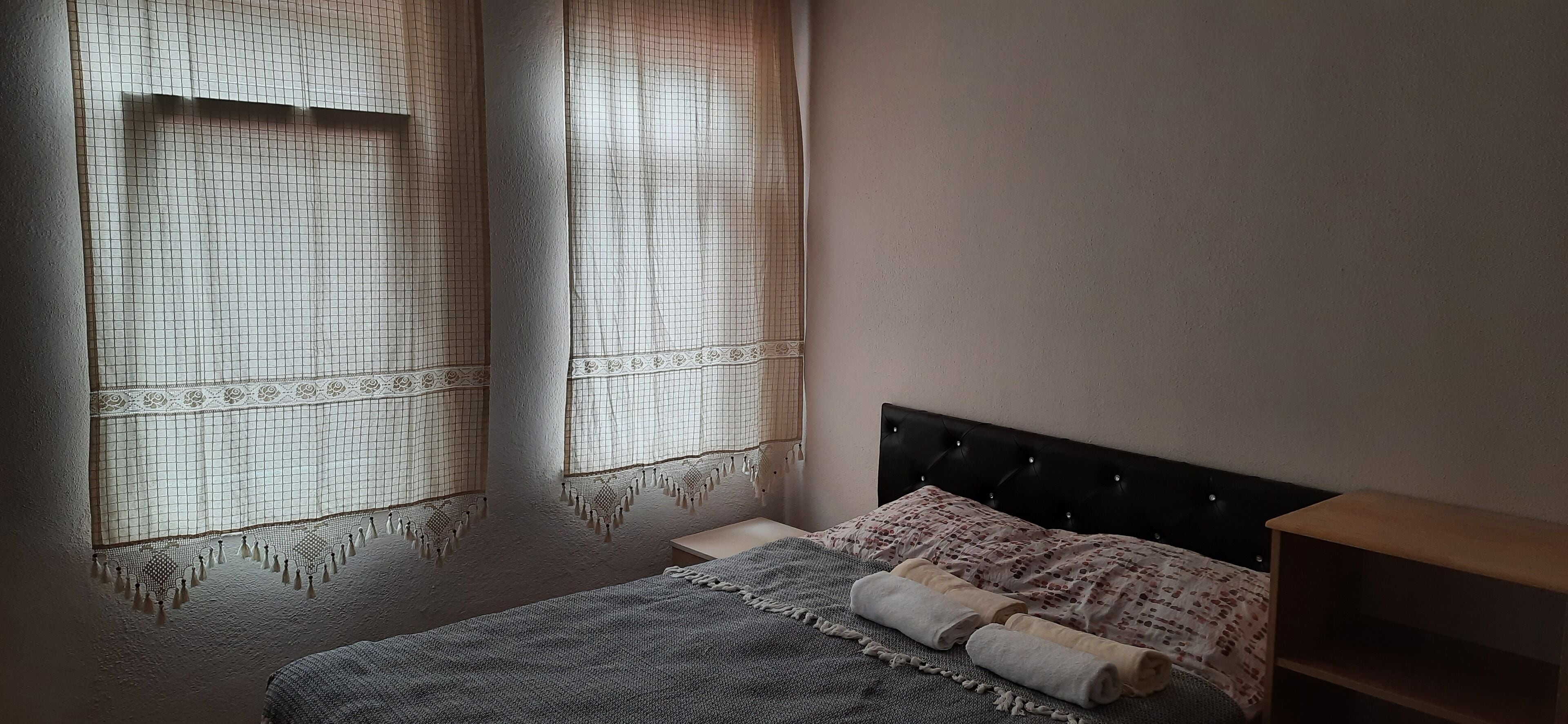 A bedroom with a bed, a nightstand, and a window with a patterned curtain.