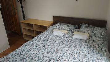 A bedroom with a bed, a wooden nightstand, a wall-mounted coat rack, and a door.